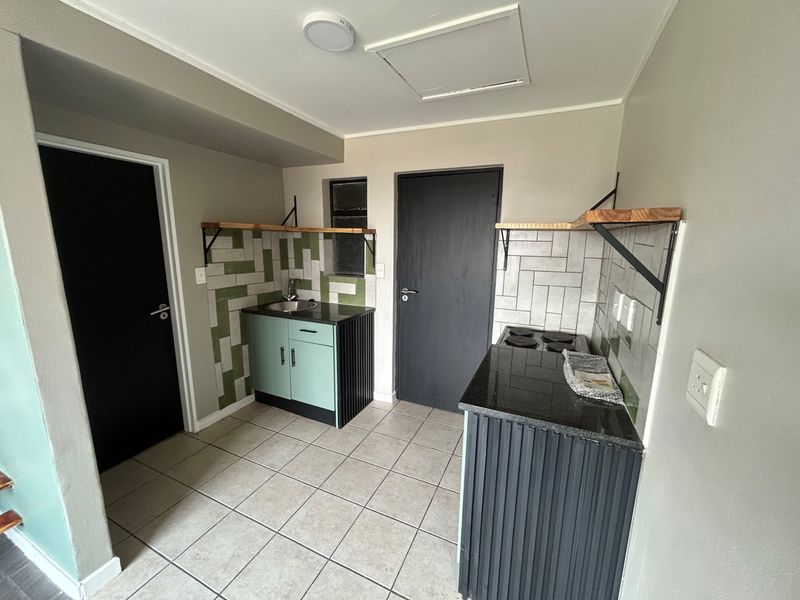 A compact kitchen featuring modern cabinetry, granite countertops, a built-in electric hob, and stylish tiled backsplashes with neutral floor tiling.