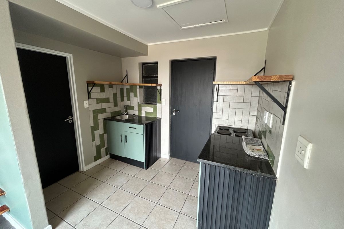 A compact kitchen featuring modern cabinetry, granite countertops, a built-in electric hob, and stylish tiled backsplashes with neutral floor tiling.