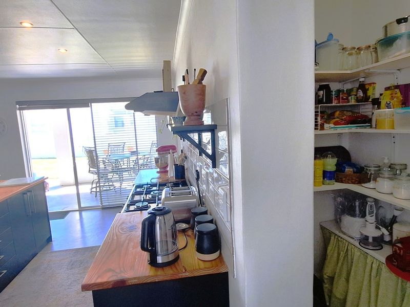A functional kitchen featuring timber countertops, a gas hob with extractor, subway tile splashback, and an integrated walk-in pantry with ample shelving.