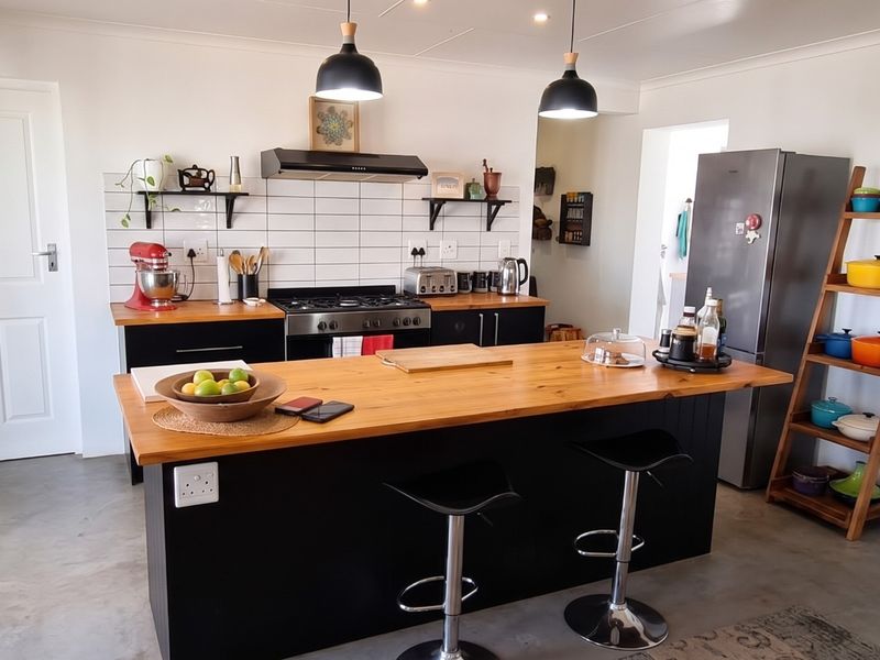 Modern kitchen featuring a central island with wooden countertop, gas hob, subway tile backsplash, and polished concrete flooring.
