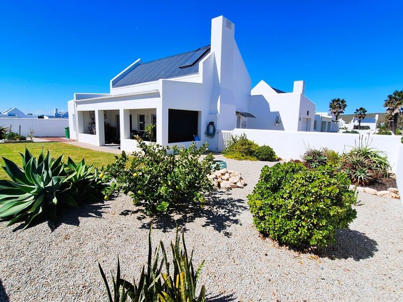 Rear view of a white-walled house featuring a covered patio, metal roof, chimney, and a well-maintained garden with gravel landscaping.