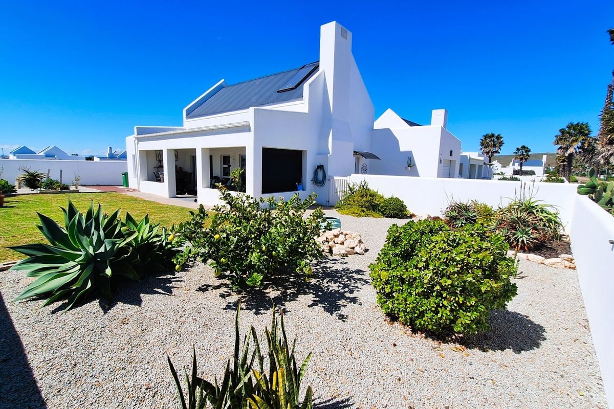 Rear view of a white-walled house featuring a covered patio, metal roof, chimney, and a well-maintained garden with gravel landscaping.