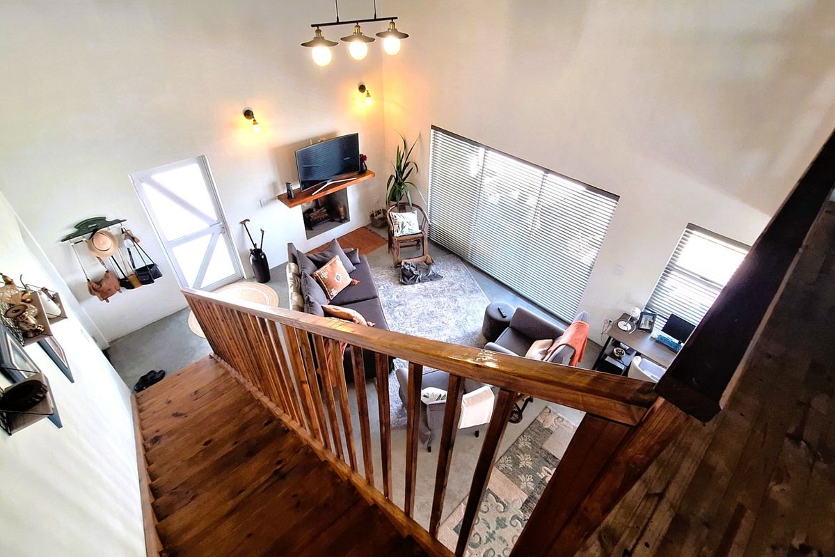High-angle view of a living room featuring a wooden staircase, fireplace with mantelpiece, and large windows with venetian blinds.