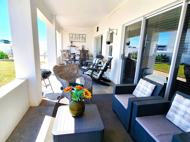 A spacious covered patio featuring concrete flooring and large sliding glass doors, providing seamless access to the garden area.