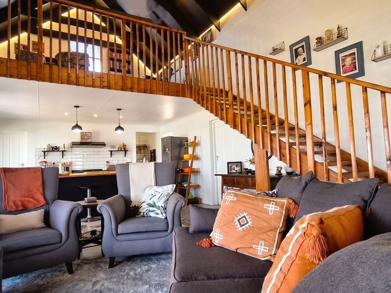 Spacious open-plan living area featuring a striking timber staircase, vaulted ceilings with exposed rafters, and a modern kitchen with subway tile backsplash.
