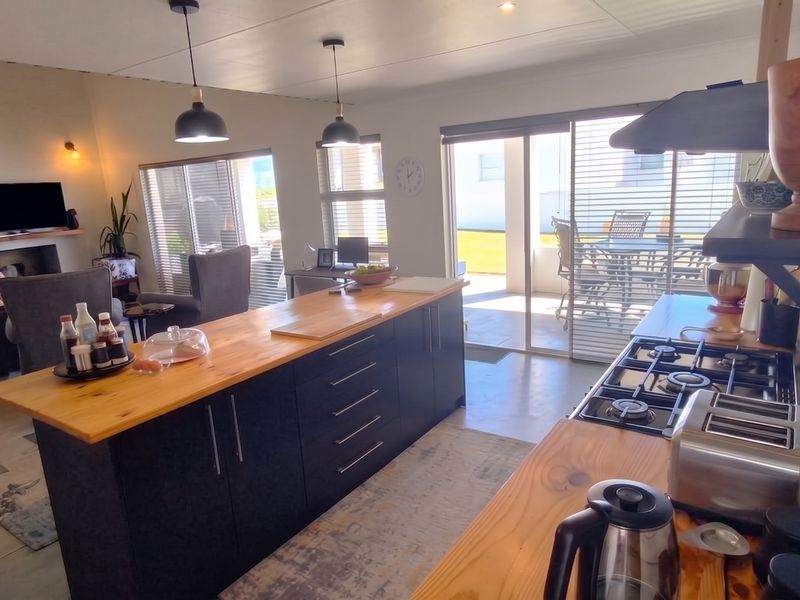 Modern open-plan living area featuring a kitchen island with timber countertops, gas hob, and seamless flow to the outdoor patio through sliding glass doors.
