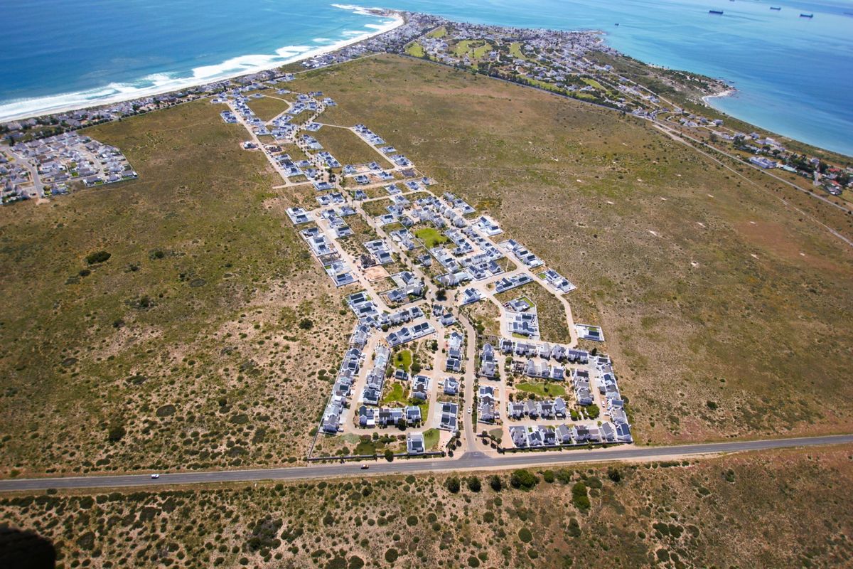 An aerial view of a coastal residential estate, showcasing the layout of the properties, road infrastructure, and proximity to the ocean.