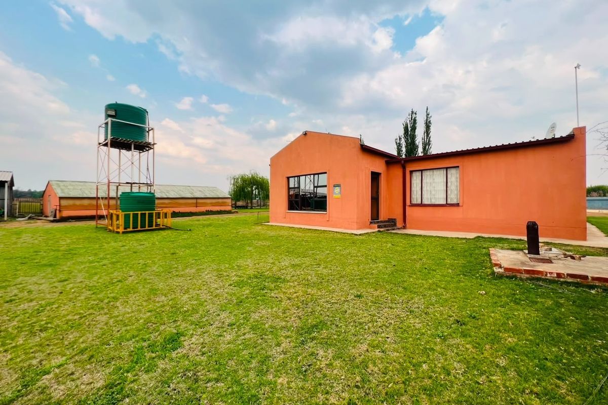 Rear view of a single-story house featuring plastered walls, aluminum windows, and an elevated water storage tank system on a large grassed yard.