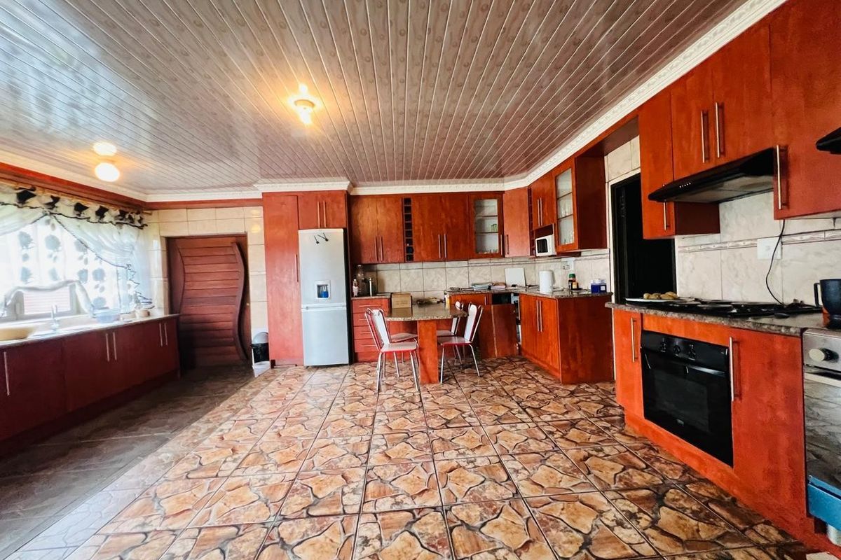 Spacious kitchen featuring extensive wooden cabinetry, built-in oven, hob, extractor fan, and distinctive tiled flooring with a classic layout.