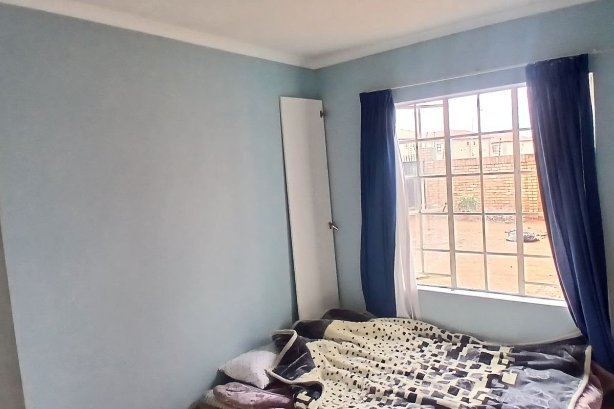 A standard bedroom featuring a window with security burglar bars and a built-in cupboard, providing a functional living space.