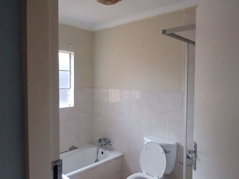 A functional bathroom featuring a bathtub, toilet, and shower area with neutral wall tiles and natural light from a side window.
