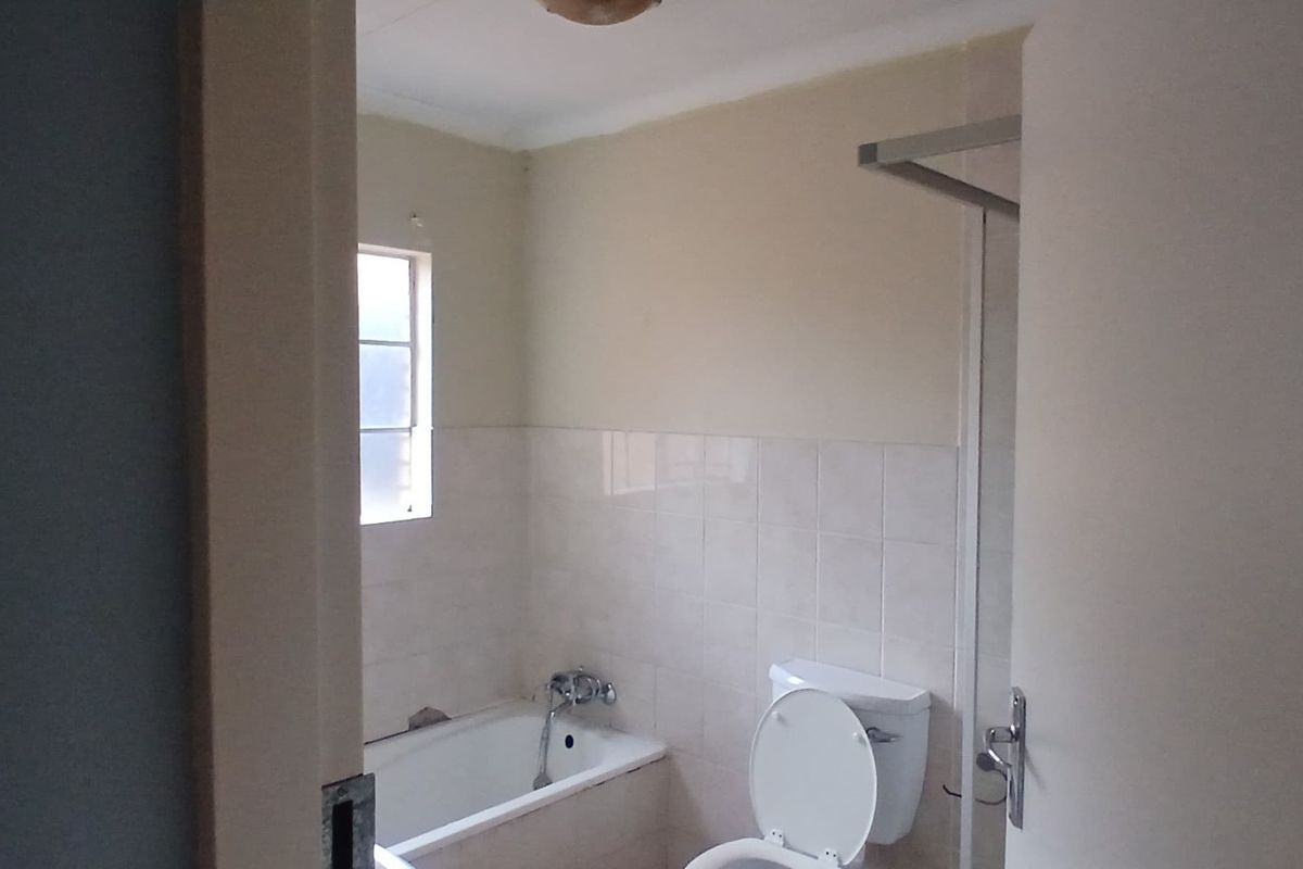 A functional bathroom featuring a bathtub, toilet, and shower area with neutral wall tiles and natural light from a side window.