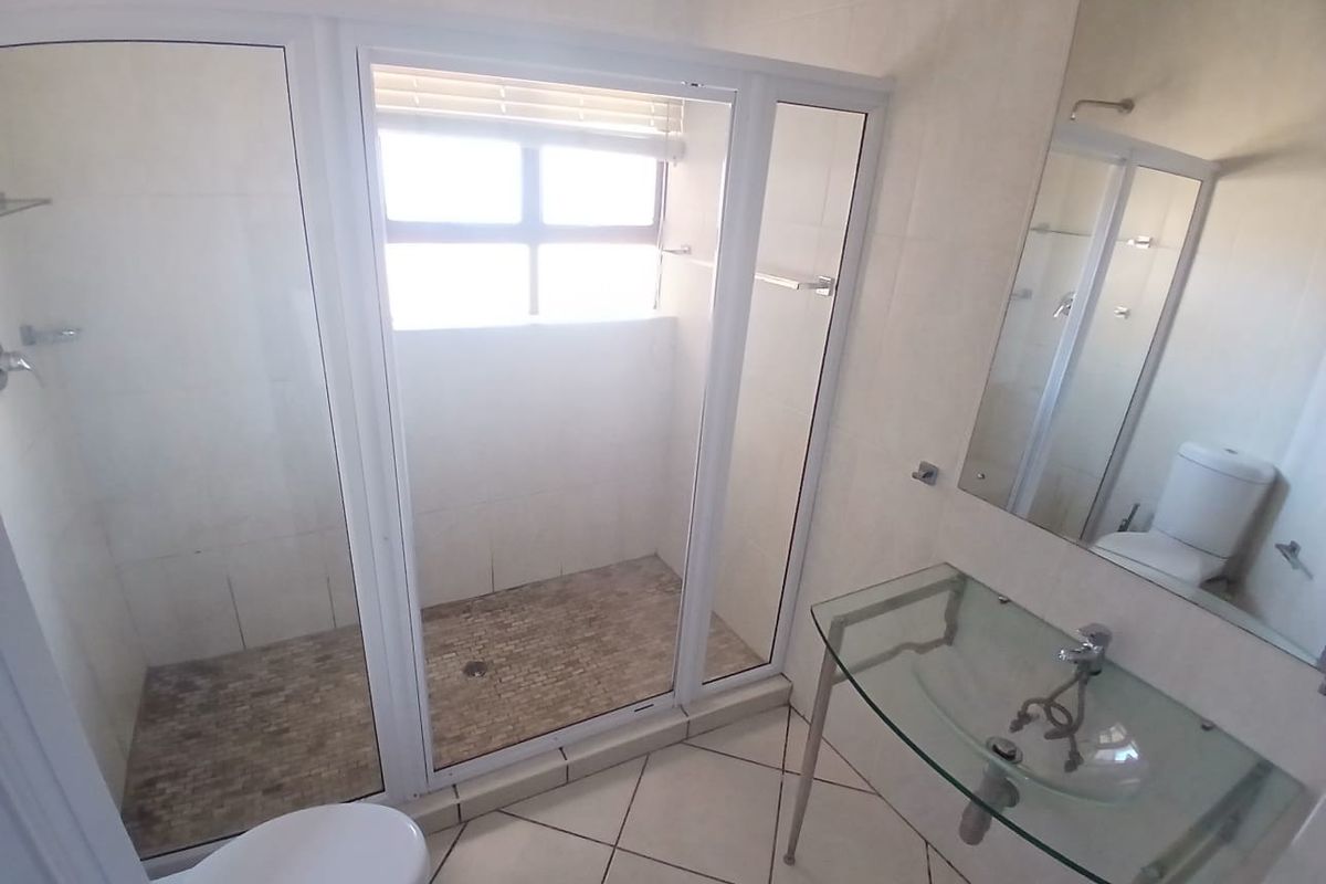 A clean, modern bathroom featuring a walk-in shower with mosaic tiling, a glass vanity basin, and a wall-mounted mirror.