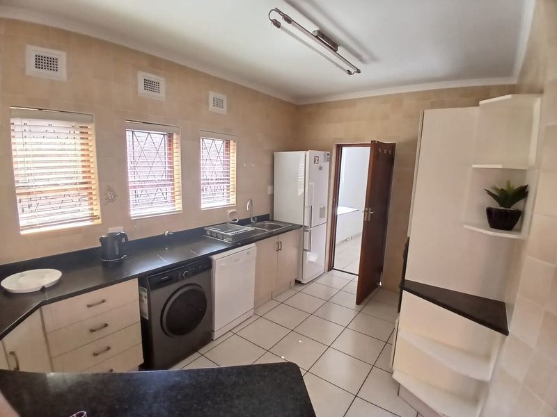 A functional kitchen featuring tiled walls and flooring, built-in cabinetry with dark countertops, and integrated space for laundry and kitchen appliances.
