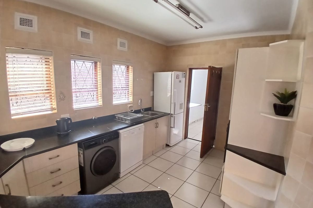 A functional kitchen featuring tiled walls and flooring, built-in cabinetry with dark countertops, and integrated space for laundry and kitchen appliances.
