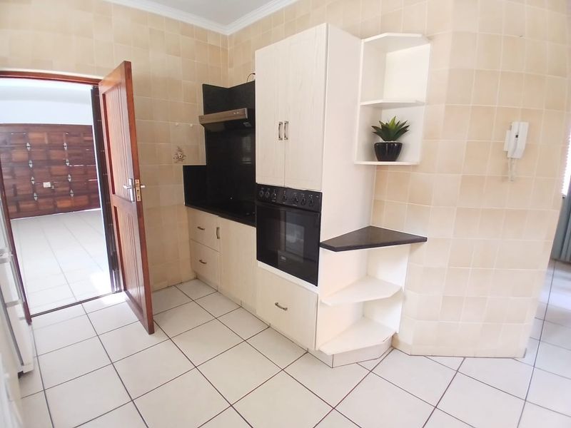 A functional kitchen area featuring built-in cabinetry, an integrated oven, extractor fan, and neutral tiled finishes throughout.
