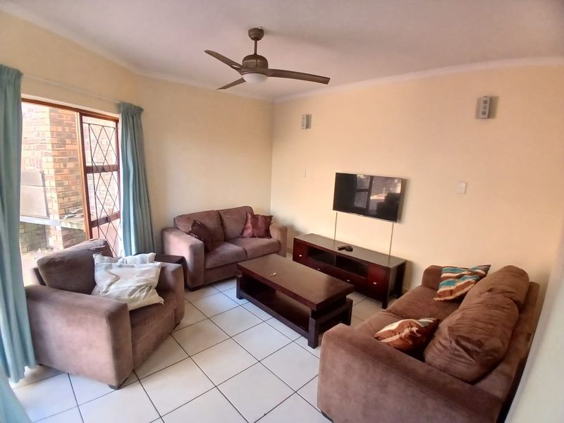 A functional living room featuring tiled flooring, a ceiling fan, and a sliding door providing access to the outdoor area.