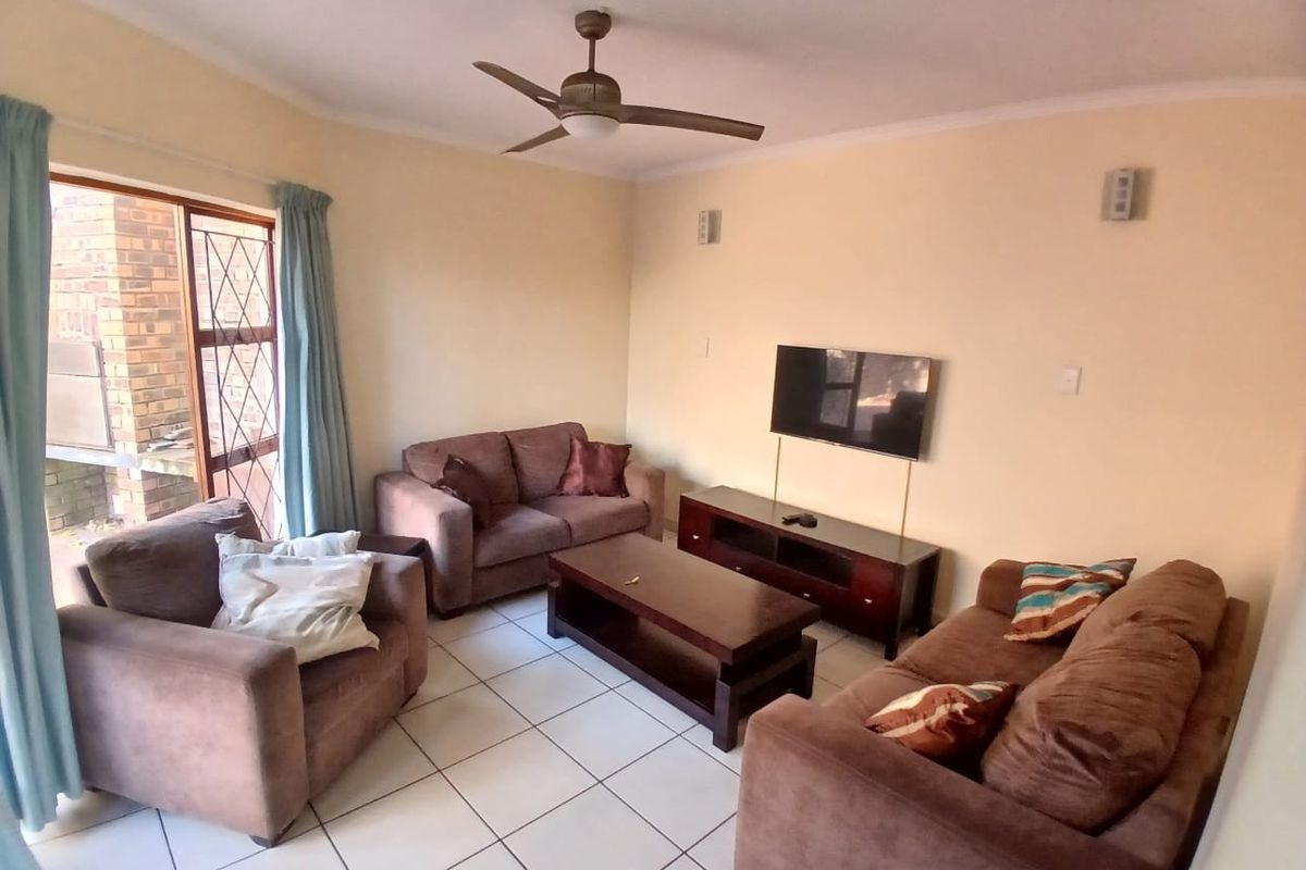 A functional living room featuring tiled flooring, a ceiling fan, and a sliding door providing access to the outdoor area.
