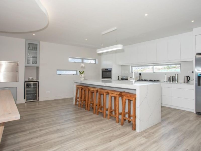 Modern open-plan kitchen featuring a large stone waterfall island, sleek white cabinetry, built-in appliances, and high-quality laminate flooring.