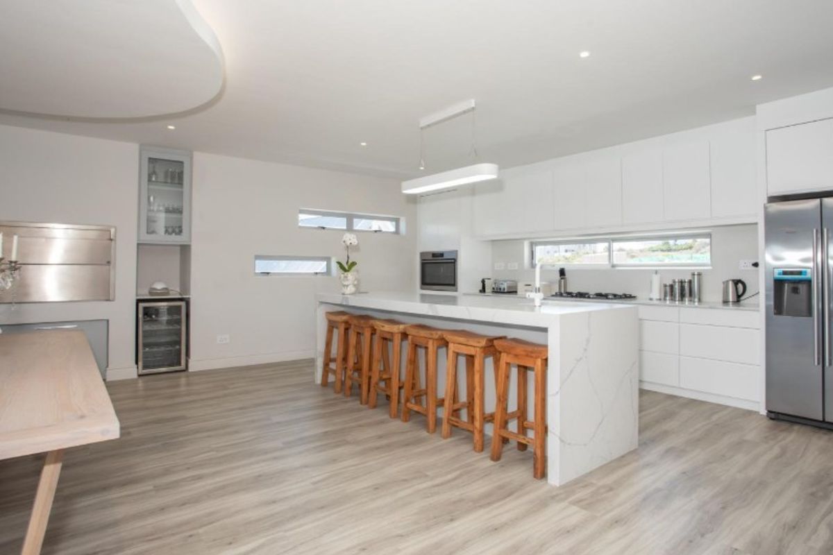 Modern open-plan kitchen featuring a large stone waterfall island, sleek white cabinetry, built-in appliances, and high-quality laminate flooring.