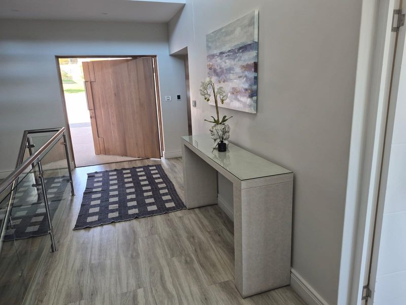 Modern entrance foyer featuring a large timber pivot door, glass balustrade staircase, and light-toned laminate flooring.