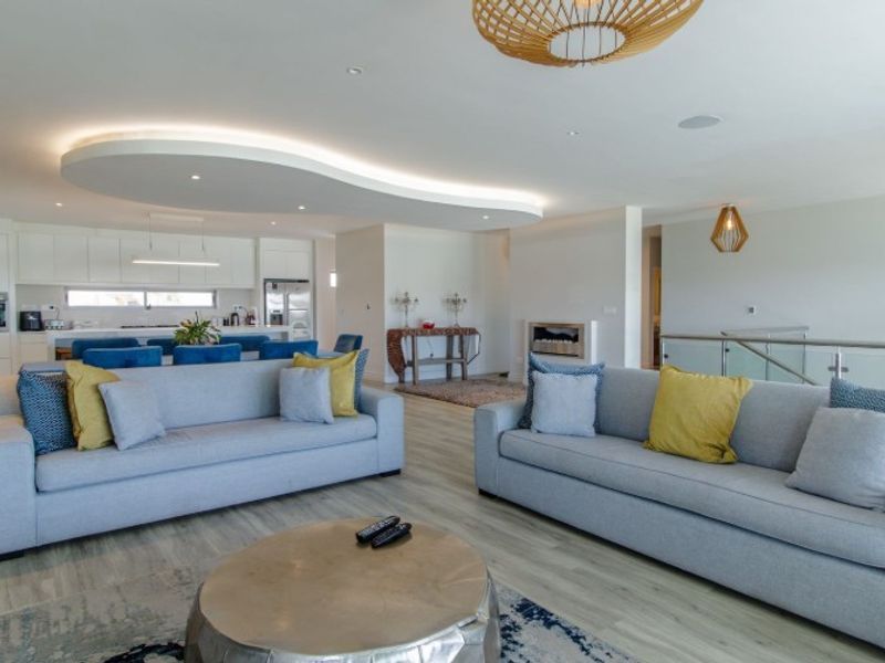 Spacious open-plan living area featuring a modern kitchen, recessed ceiling with ambient cove lighting, glass balustrade, and high-quality laminate flooring.