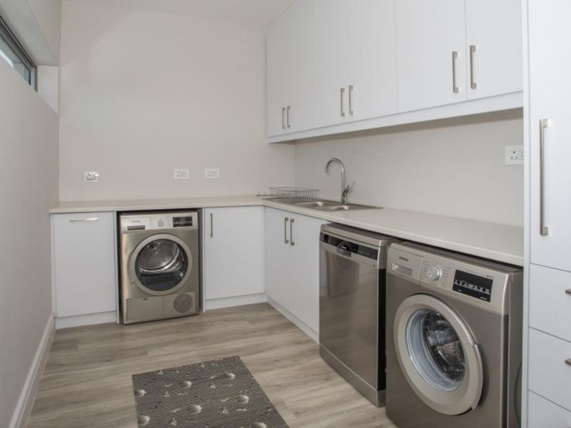 A clean and functional laundry room featuring white built-in cabinetry, laminate countertops, a stainless steel sink, and modern laminate flooring.
