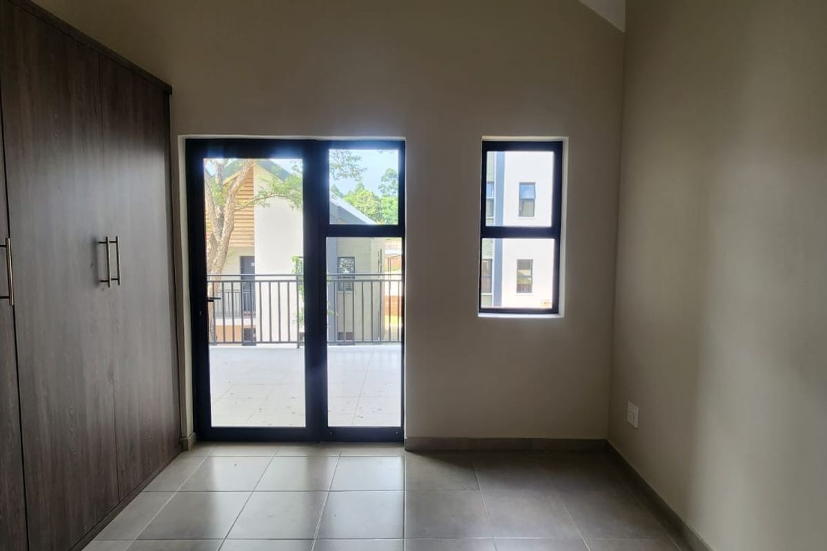 A bright, modern bedroom featuring built-in cupboards, tiled flooring, and direct access to a private balcony through a glass door.