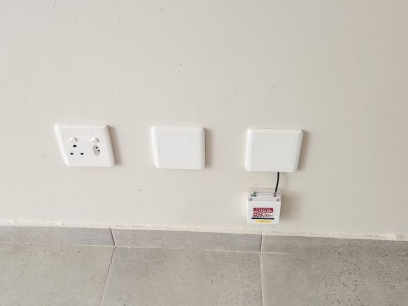 A close-up view of a wall featuring electrical outlets, data points, and a fiber optic connection box installed above tiled flooring.