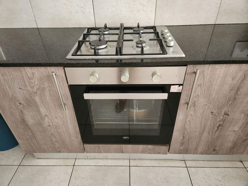A modern kitchen section featuring a built-in gas hob, stainless steel oven, granite countertops, and wood-look cabinetry with a tiled backsplash.