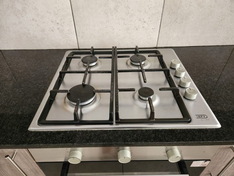 A close-up view of a stainless steel four-burner gas hob integrated into a dark granite countertop with a tiled splashback.