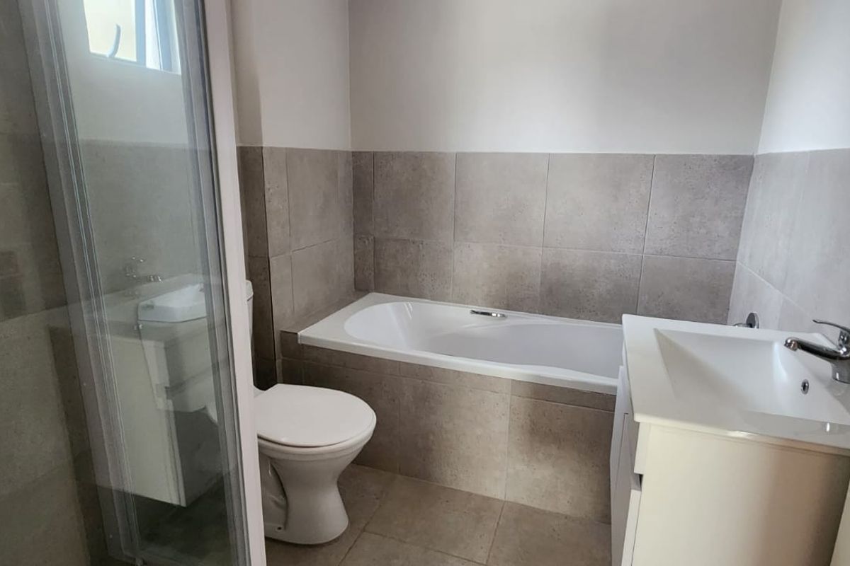 A clean, modern bathroom featuring a built-in bathtub, separate shower enclosure, vanity basin, and neutral tiled finishes.