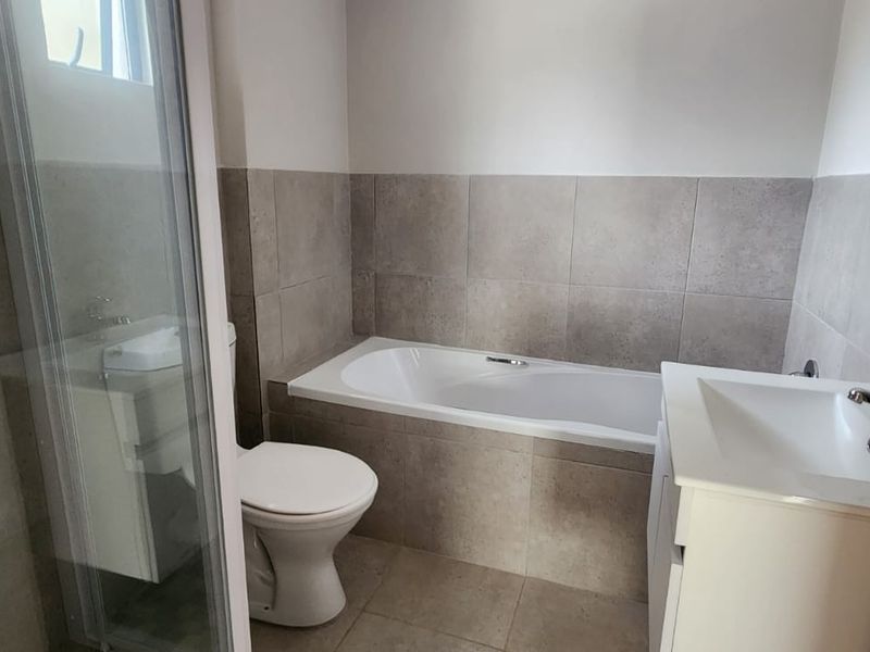 A clean, modern bathroom featuring a built-in bathtub, separate shower enclosure, vanity basin, and neutral tiled finishes.