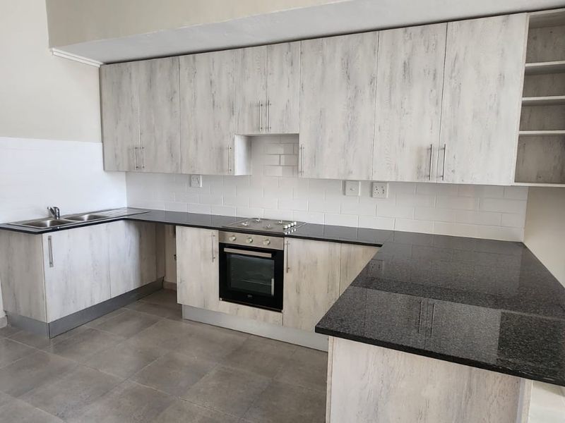 Modern kitchen featuring light wood-grain cabinetry, dark granite countertops, built-in oven, electric hob, and a clean subway tile backsplash.