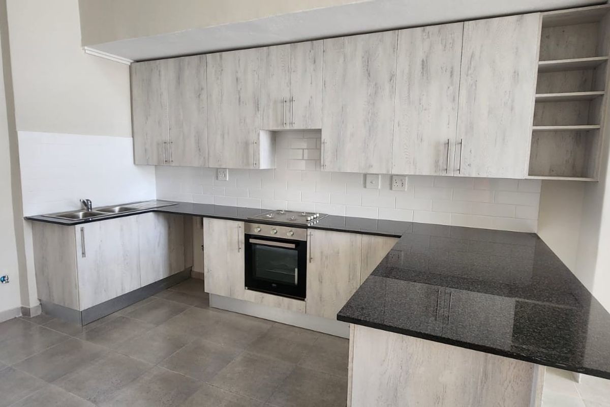 Modern kitchen featuring light wood-grain cabinetry, dark granite countertops, built-in oven, electric hob, and a clean subway tile backsplash.