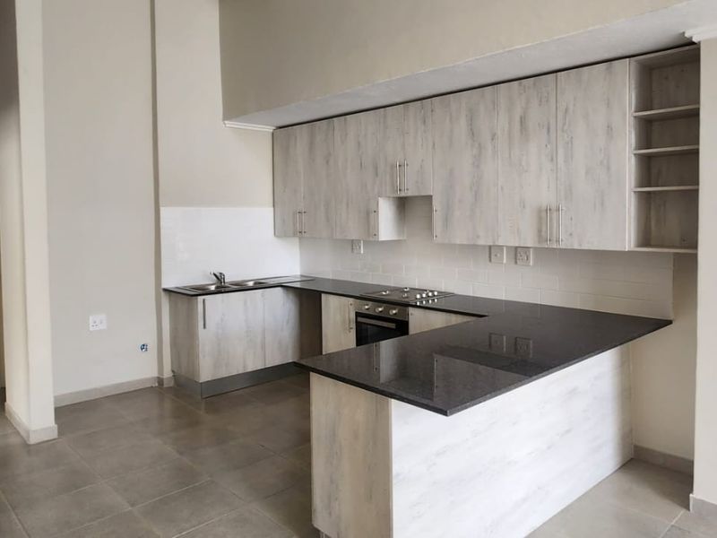 Modern kitchen featuring light wood-grain cabinetry, dark granite countertops, built-in oven, electric hob, and neutral tiled flooring in an open-plan layout.