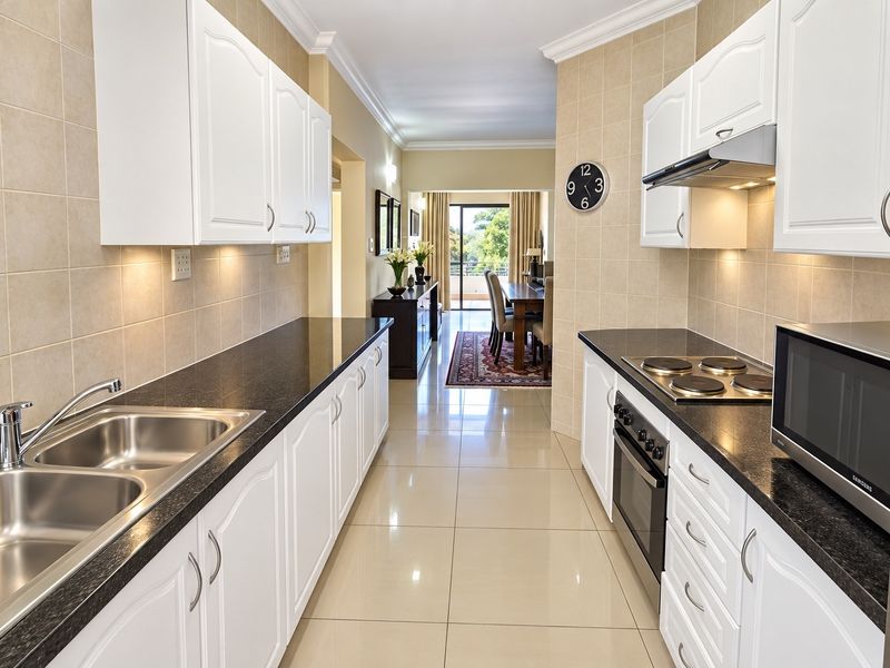 A well-maintained galley kitchen featuring white cabinetry, granite countertops, built-in oven, hob, and extractor fan, leading through to an open-plan dining area.