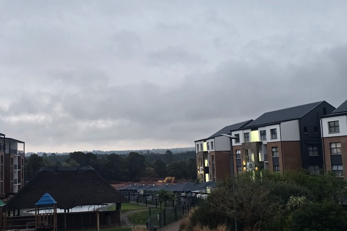 Exterior view of a residential apartment complex featuring landscaped grounds, a thatched lapa, and covered parking facilities under an overcast sky.