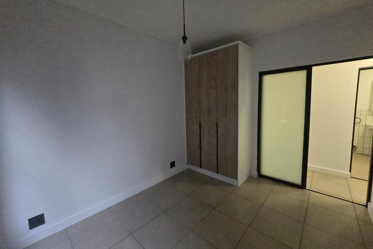 A clean, empty bedroom featuring neutral tiled flooring, a modern built-in wardrobe, and a sliding door leading to an adjacent space.