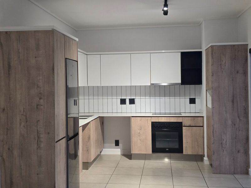 Modern kitchen featuring wood-grain and white cabinetry, integrated oven and hob, tiled backsplash, and neutral floor tiles in a clean, contemporary layout.