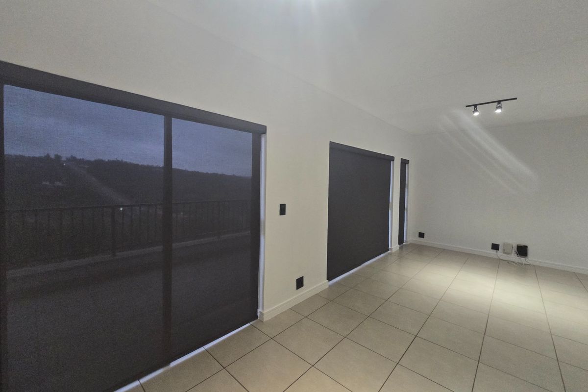 Spacious, empty living area featuring neutral ceramic floor tiles, modern track lighting, and large sliding glass doors with roller blinds leading to a balcony.