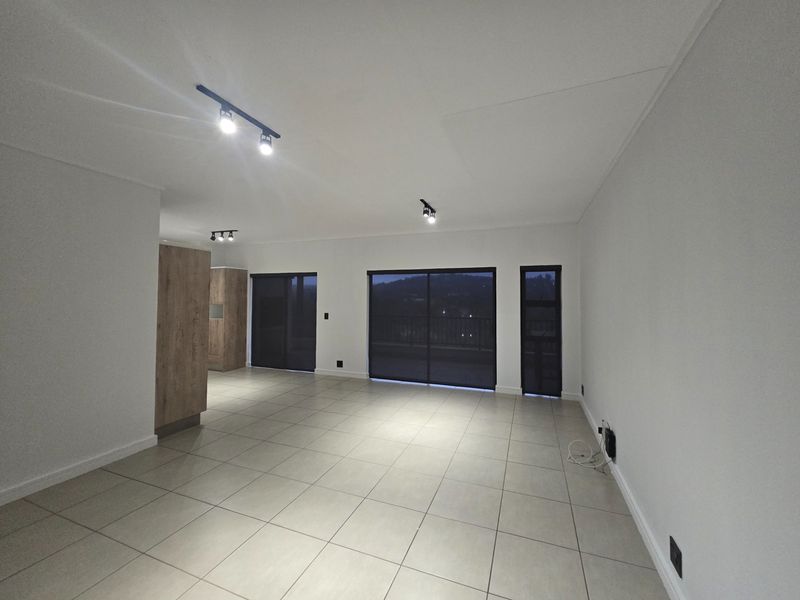 Spacious open-plan living area featuring neutral tiled flooring, modern track lighting, and large sliding glass doors leading to an outdoor space.