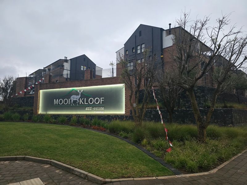 The entrance to Mooikloof Eco-Estate featuring modern multi-story apartment buildings, illuminated signage, and well-maintained landscaped grounds.