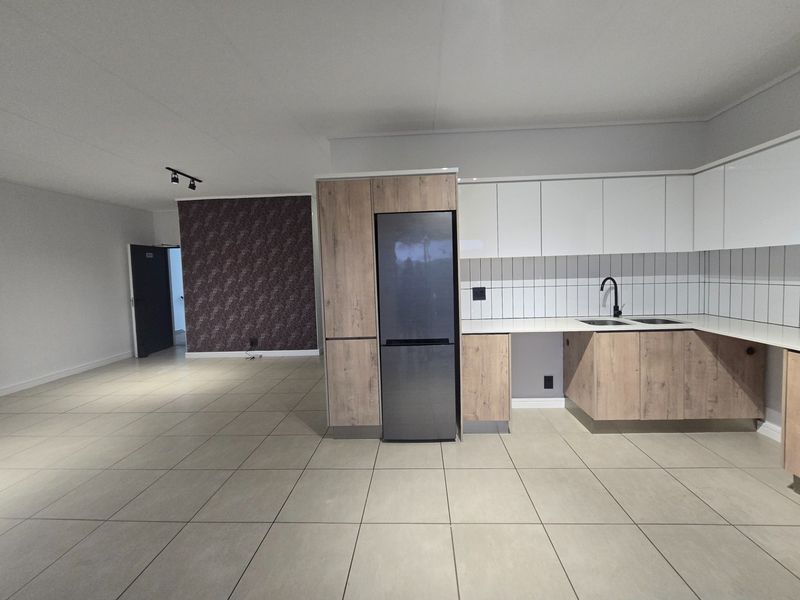 Modern open-plan kitchen and living area featuring contemporary two-tone cabinetry, tiled flooring, and sleek black fixtures in a spacious, well-lit layout.