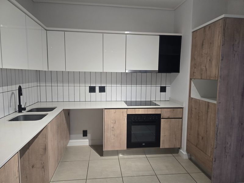 Modern kitchen featuring sleek white and wood-grain cabinetry, quartz countertops, integrated appliances, and a stylish tiled backsplash.