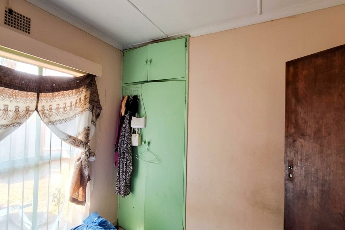 A bedroom featuring a built-in wardrobe with green cabinetry and a ceiling ventilation vent, requiring cosmetic updates to improve the overall aesthetic.