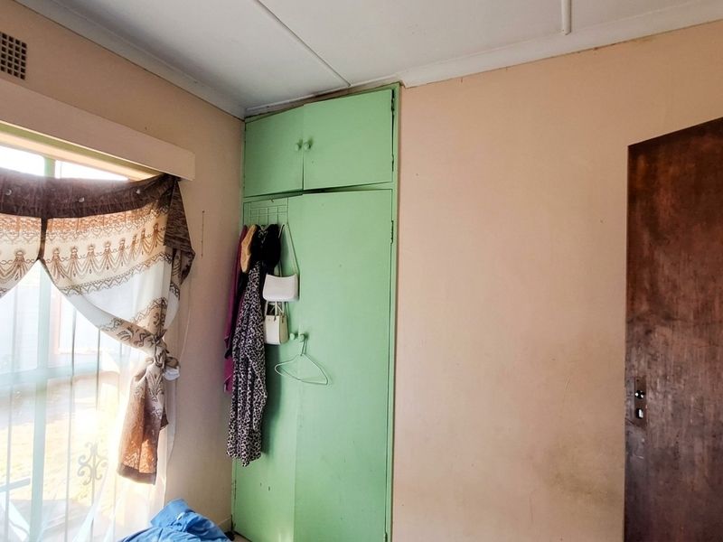 A bedroom featuring a built-in wardrobe with green cabinetry and a ceiling ventilation vent, requiring cosmetic updates to improve the overall aesthetic.