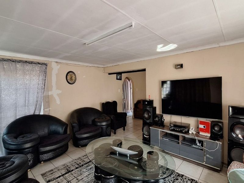 A living room featuring tiled flooring and an arched doorway, currently showing signs of wear on the walls and ceiling requiring cosmetic attention.