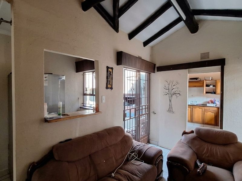 Open plan living area featuring exposed timber ceiling beams, a convenient serving hatch to the kitchen, and direct access to the exterior via a security gate.