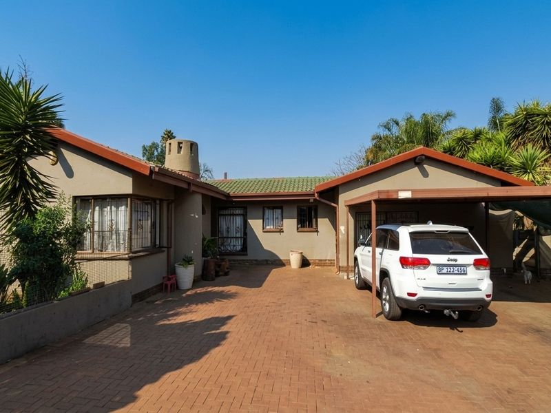 Front exterior view of a single-story house featuring a paved driveway, attached carport, and traditional tiled roof architecture.